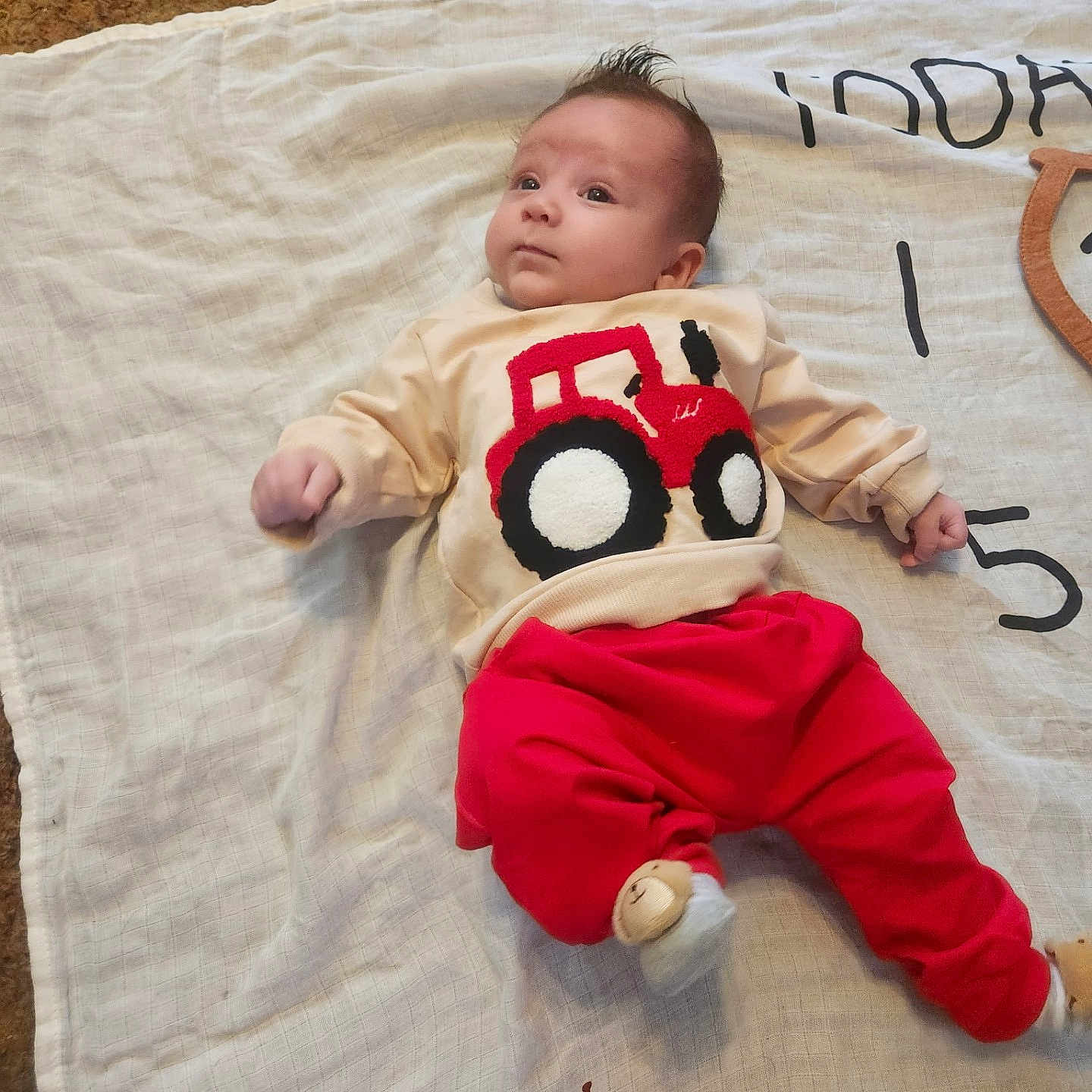 Beau Wesley Graham is registered to the contest to win money with this photo: baby, blanket, carpet, child, clothing, cute, expression, face, floor, giraffe_print, indoors, infant, lying_down, portrait, red_pants, soft_lighting, sweater, toy_sock, tractor_design, young