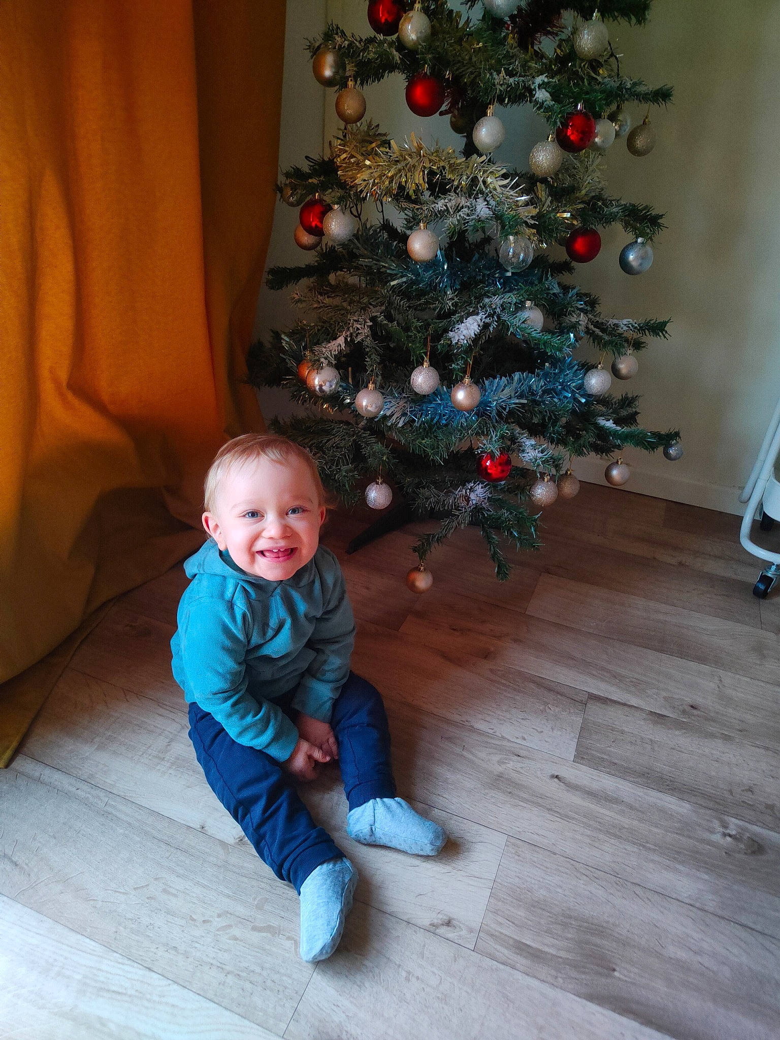 Marlon a rejoint le concours — aidez-le/la à gagner de superbes lots ! baby_toddler_clothing, christmas, christmas_decoration, christmas_ornament, christmas_tree, comfort, conifer, event, flooring, happy, hardwood, holiday, holiday_ornament, joy, ornament, person, plant, smile, standing, toddler