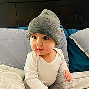 Isaac is registered to the contest to win money with this photo: baby, child, beanie, hat, white_clothing, gray_clothing, bed, pillow, blanket, indoor, curious, cute, infant, portrait, sitting, soft_lighting, headwear, couch, young_child, person