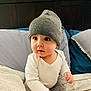 baby, child, beanie, hat, white_clothing, gray_clothing, bed, pillow, blanket, indoor, curious, cute, infant, portrait, sitting, soft_lighting, headwear, couch, young_child, person