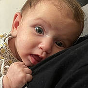 Lola a rejoint le concours — aidez-le/la à gagner de superbes lots ! baby, infant, close_up, face, hand, skin, eyes, curious, resting, fabric, black_clothing, portrait, cute, young_child, human, expression, soft_light, indoors, casual, tender_moment