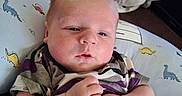 Oaklei Storm is registered to the contest to win money with this photo: baby, infant, blanket, pillow, dinosaur_pattern, clothing, hand, face, person, indoor, carpet, soft_toys, cute, newborn, resting, comfort, portrait, child, sleepy, casual