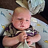 baby, infant, blanket, pillow, dinosaur_pattern, clothing, hand, face, person, indoor, carpet, soft_toys, cute, newborn, resting, comfort, portrait, child, sleepy, casual