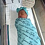 Zaeana is registered to the contest to win money with this photo: newborn, baby, swaddle, headband, sleeping, hospital_bassinet, footprints, birth_details, blanket, infant, person, resting, wrapped, blue, text, cloth, bed, cute, peaceful, indoor