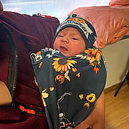 Zaeana is registered to the contest to win money with this photo: newborn, baby, infant, child, halloween, blanket, hat, person, hand, maroon_jacket, face, indoors, bed, pillow, wooden_floor, holding, cozy, cute, wrapped, portrait