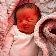 Ronnie is registered to the contest to win money with this photo: baby, newborn, infant, smile, sleeping, blanket, soft_texture, pink, gray, white_clothing, cozy, closeup, peaceful, portrait, child, human, cute, resting, warm_light, indoor