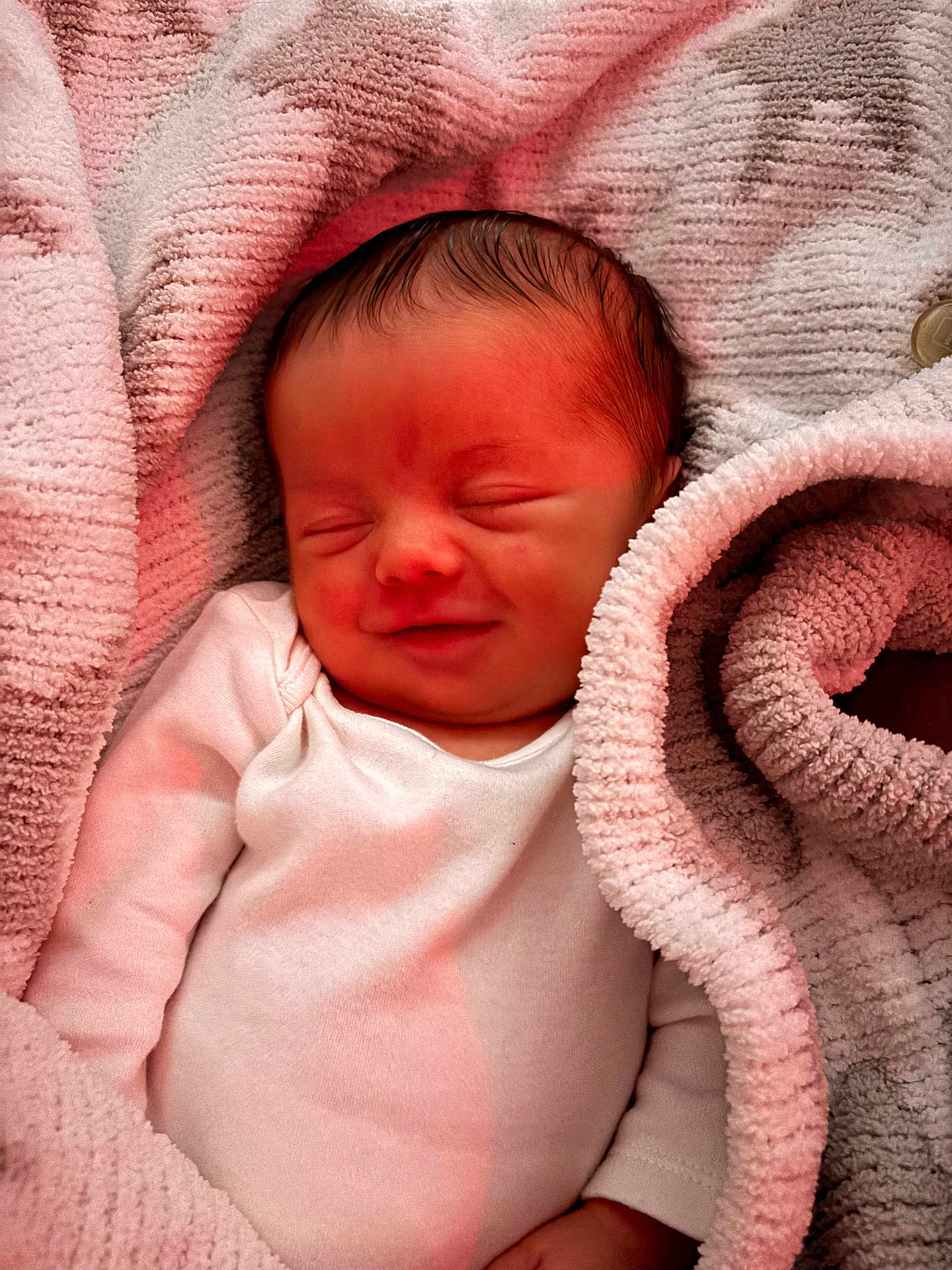 Ronnie is registered to the contest to win money with this photo: baby, newborn, infant, smile, sleeping, blanket, soft_texture, pink, gray, white_clothing, cozy, closeup, peaceful, portrait, child, human, cute, resting, warm_light, indoor