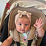 Laura is registered to the contest to win money with this photo: baby, child, blue_eyes, bow, car_seat, child_seat, clothing, cute, dress, floral_pattern, headband, infant, indoors, pacifier_clip, person, portrait, raising_hand, seatbelt, smiling, straps