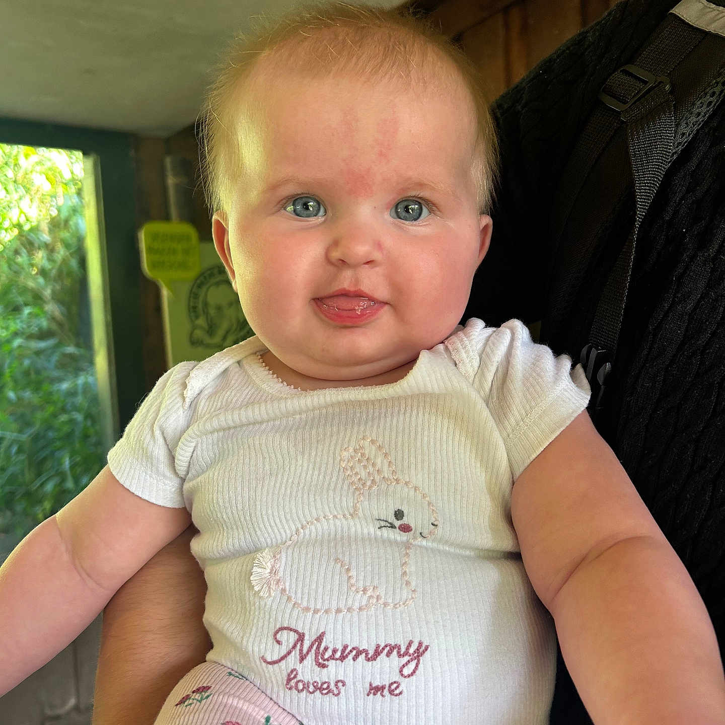 Laura joined the competition — help win amazing prizes! baby, blue_eyes, bunny_design, child, cute, face, floral_pattern, greenery, holding, indoor, infant, person, pink_pants, short_hair, skin, smiling, text_on_clothing, tongue, white_shirt, window