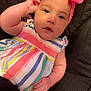 baby, infant, child, pink_bow, headband, striped_dress, colorful_clothing, cute, chubby_cheeks, hand, face, eyes, lying_down, fabric, dark_background, portrait, skin, baby_fashion, cute_expression, child_portrait
