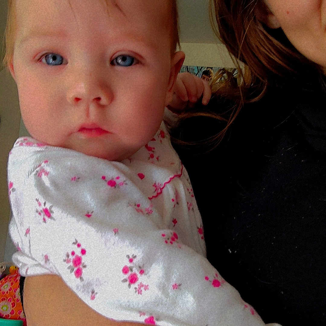 Stormy joined the competition — help win amazing prizes! adult, baby, blue_eyes, calm, child, close_up, curious, face, hair, hand, holding, indoor, infant, looking_at_camera, person, pink_flowers, portrait, skin, toddler, white_clothing