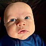 baby, close_up, face, blue_eyes, infant, child, portrait, clothing, quilted_background, expression, cute, young_child, indoor, person, head, skin, eyelashes, nose, mouth, soft_lighting