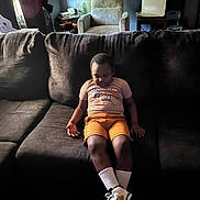 Adrian joined the competition — help win amazing prizes! child, boy, sitting, couch, living_room, casual_clothing, shorts, tshirt, sneakers, white_socks, indoor, furniture, armchair, table, air_purifier, window, curtains, relaxed, quiet, home