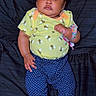 baby, infant, child, cute, lying_down, yellow_shirt, bee_pattern, blue_pants, polka_dot, bow, wristband, barefoot, black_background, portrait, indoors, skin, face, hands, feet, clothing
