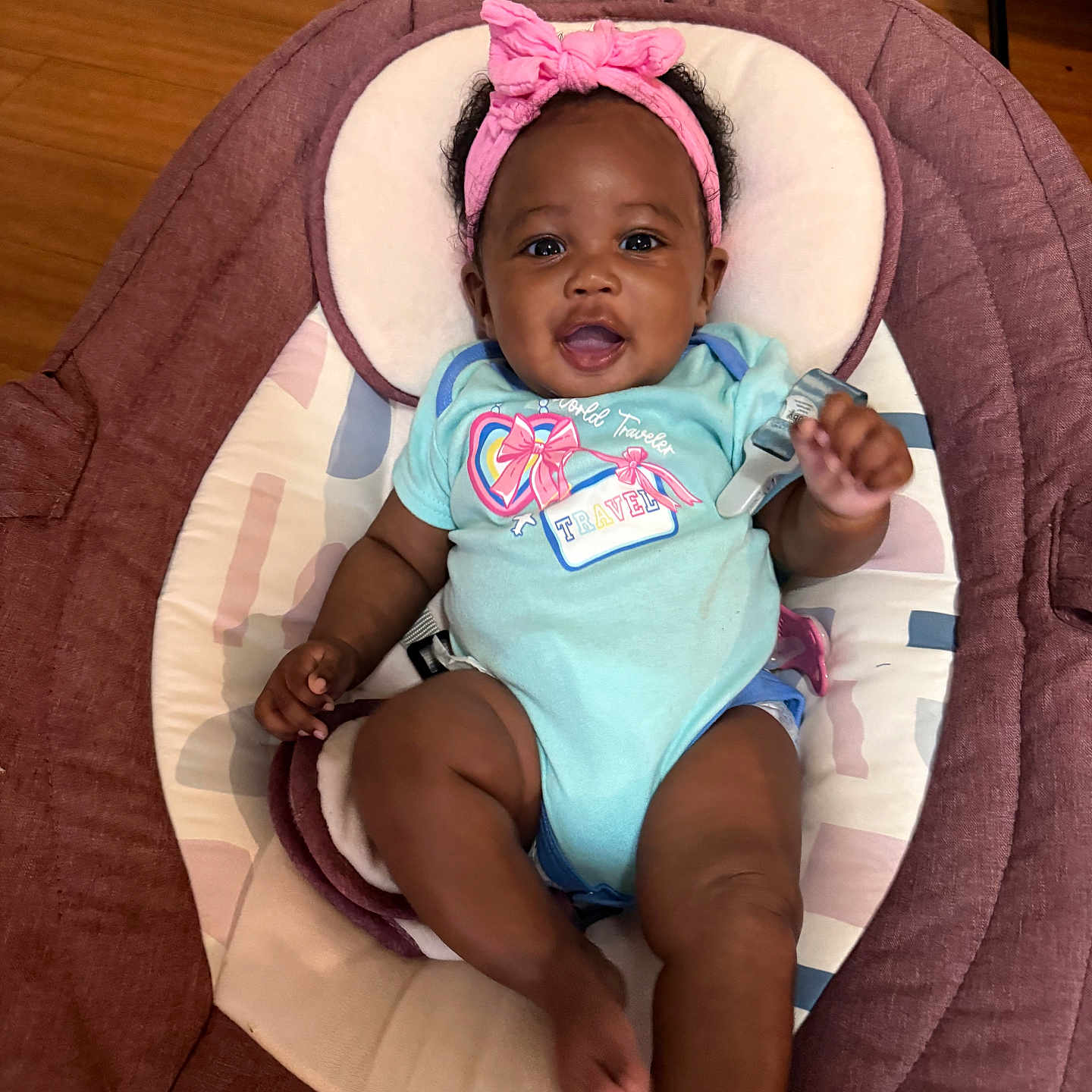 Aliya is registered to the contest to win money with this photo: baby, infant, smiling, headband, onesie, baby_seat, cushion, happy, child, person, indoors, floor, wooden_floor, pink, blue, cute, portrait, young_child, clothing, relaxing