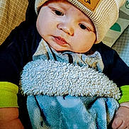Jason is registered to the contest to win money with this photo: baby, child, hat, beanie, blanket, blue_blanket, dinosaur_patch, face, infant, cute, cozy, warm_clothing, pout, hand, soft_texture, indoors, person, young_child, apparel, portrait