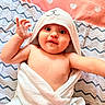 baby, infant, child, portrait, smiling, waving, hooded_towel, bathrobe, blanket, bedding, heart_pattern, bed, lying_down, indoor, close_up, face, eyes, hands, cozy, photography