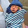 newborn, baby, sleeping, hat, blue, striped_blanket, leaf, hand, adult, holding, cozy, closeup, portrait, soft_focus, outdoor, skin, face, peaceful, infant, wrapped