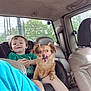 child, dog, car_seat, vehicle_interior, window, tree, greenery, smile, pet, seatbelt, happy, leather_seat, casual_clothing, tongue_out, car, backseat, young_child, candid, indoor, transportation