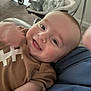 Ash joined the competition — help win amazing prizes! baby, smiling, infant, face, brown_shirt, football_design, person, indoors, carpet, blue_cloth, stroller, blurred_background, happy, cute, toddler, skin, head, eyes, mouth, arm