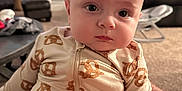Ash joined the competition — help win amazing prizes! baby, infant, onesie, pretzel_pattern, indoor, living_room, carpet, sofa, table, face, person, child, cute, seated, clothing, home, expression, curious, soft_light, portrait
