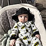 Ash is registered to the contest to win money with this photo: baby, batman, onesie, hood, bat_ears, cushion, baby_seat, plush_toy, carpet, indoor, child, cute, infant, portrait, clothing, sitting, hand, face, eyes, soft_toy