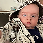 Ash is registered to the contest to win money with this photo: baby, child, indoor, couch, plaid, hood, jacket, blue_eyes, face, person, infant, clothing, portrait, sitting, staircase, home, cozy, young_child, looking_at_camera, casual