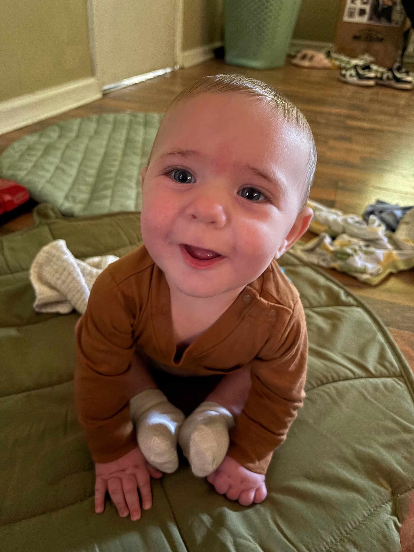 Kanen is registered to the contest to win money with this photo: baby, child, smiling, crawling, indoor, brown_clothing, white_socks, floor, mat, quilted, happy, infant, hands, feet, face, person, home, wooden_floor, cozy, cute