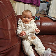 Annika is registered to the contest to win money with this photo: baby, child, couch, leather, onesie, socks, remote_control, door, towel, indoor, furniture, person, face, expression, cozy, casual, relaxed, home, infant, curious