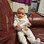 baby, child, couch, leather, onesie, socks, remote_control, door, towel, indoor, furniture, person, face, expression, cozy, casual, relaxed, home, infant, curious