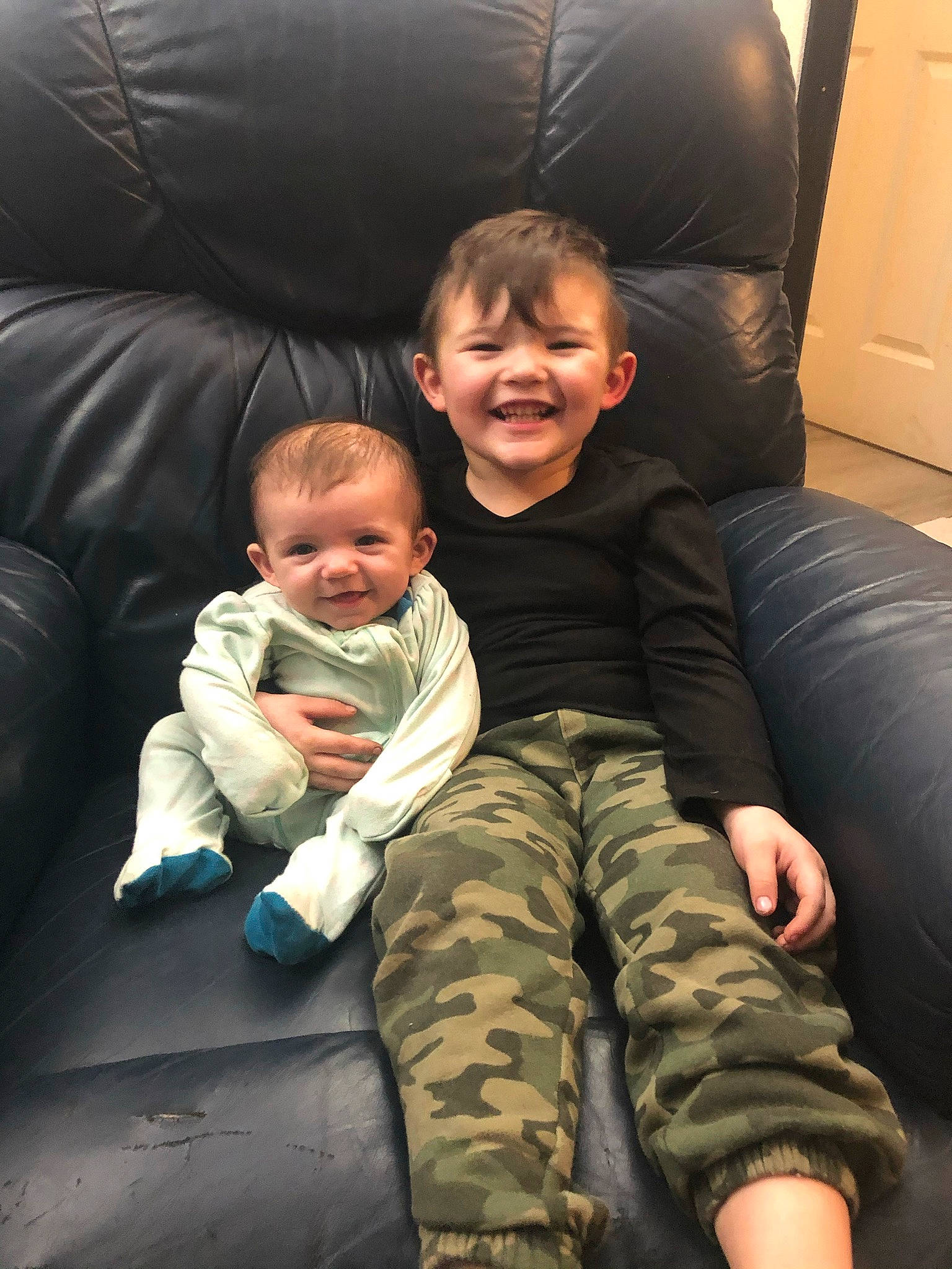 Bentley is registered to the contest to win money with this photo: arm, baby, camouflage, child, comfort, door, fun, gesture, hair, happy, human_leg, joy, lap, leg, lighting, military_camouflage, person, sitting, smile, thigh