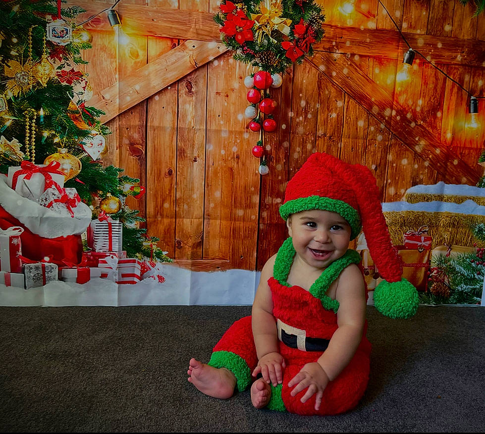 Jeziah is registered to the contest to win money with this photo: christmas, christmas_decoration, christmas_eve, christmas_ornament, christmas_tree, event, grass, happy, hat, headwear, holiday, joy, leisure, ornament, person, plant, red, smile, toddler, tradition