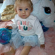 Gaïa a rejoint le concours — aidez-le/la à gagner de superbes lots ! toddler, child, blue_eyes, unicorn, plush_toy, pink_blanket, tutu_skirt, sweater, barefoot, indoor, cute, soft_texture, pastel_colors, sitting, portrait, young_child, toy, cozy, playful, innocent