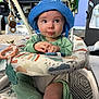 baby, blue_hat, green_pajamas, baby_seat, toy, indoor, child, cute, infant, playtime, smiling, face, hands, carpet, decor, nutcracker, plush_toy, furniture, expression, person