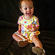 Caityy joined the competition — help win amazing prizes! baby, barefoot, bright_colors, casual_clothing, child, curly_hair, cute, flower_pattern, happy, indoors, leather_couch, person, playful, portrait, sitting, small_shoes, smiling, toddler, yellow_dress, young_child