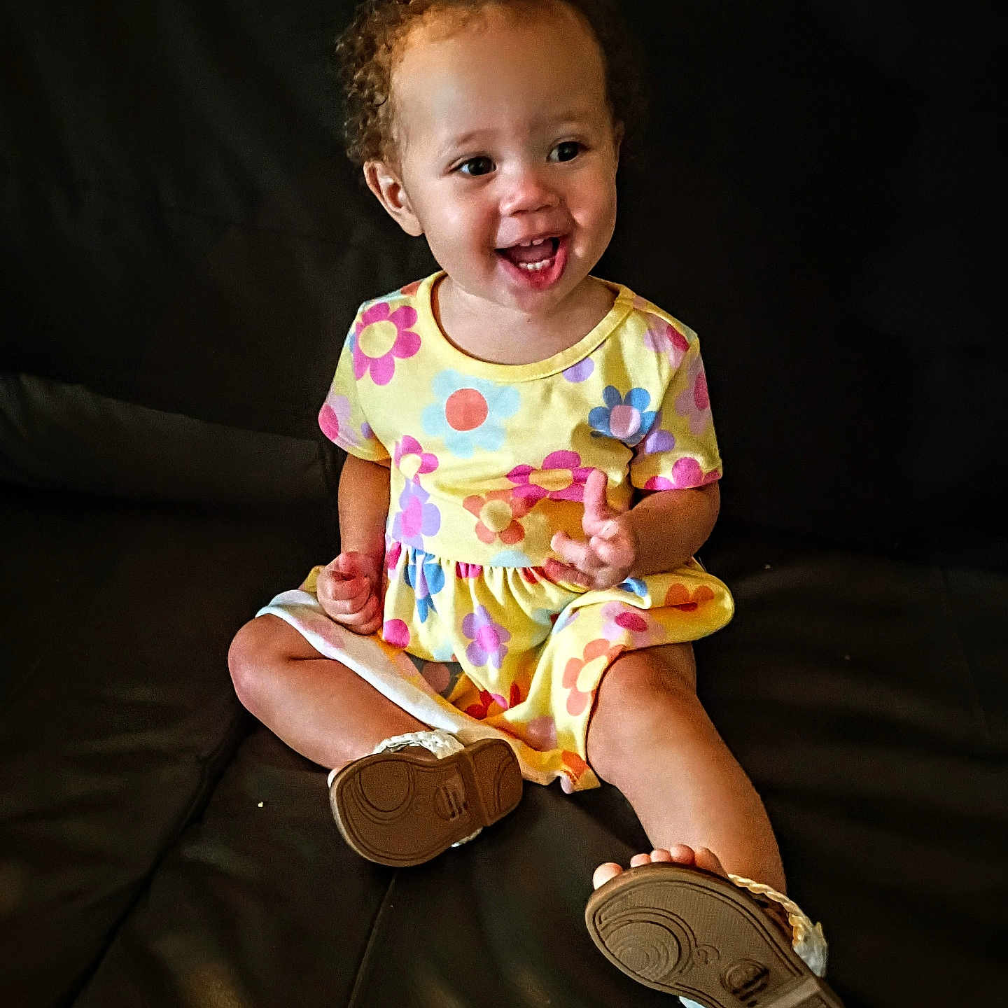 Caityy joined the competition — help win amazing prizes! baby, barefoot, bright_colors, casual_clothing, child, curly_hair, cute, flower_pattern, happy, indoors, leather_couch, person, playful, portrait, sitting, small_shoes, smiling, toddler, yellow_dress, young_child