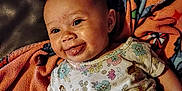 Caityy joined the competition — help win amazing prizes! baby, blanket, child, closeup, comfort, cozy, cute, expression, face, floral_onesie, happy, head, indoors, infant, lying_down, playful, skin, smiling, tongue_out, warm_lighting