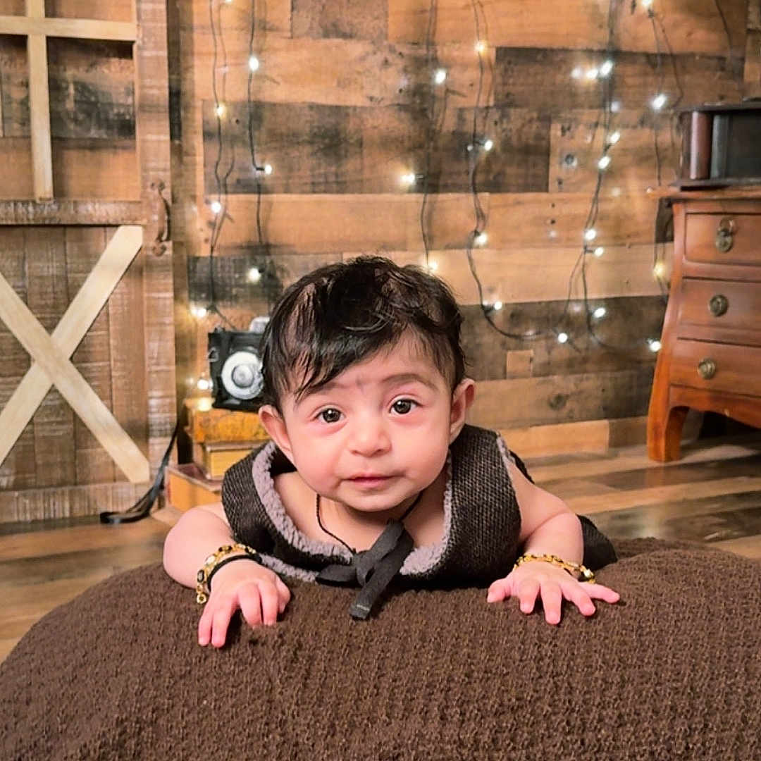 Ayzel is registered to the contest to win money with this photo: baby, child, infant, face, smiling, blanket, brown, wooden_wall, fairy_lights, bracelets, indoors, floor, furniture, drawer, portrait, cute, looking_at_camera, cozy, warm_lighting, decor