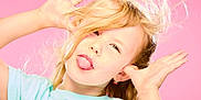 Constance participe au concours pour gagner de l'argent avec cette photo : blonde_hair, blue_shirt, casual_clothing, child, close_up, cute, earrings, expression, fun, hands_up, happy, joyful, person, pink_background, playful, portrait, silly_face, studio_lighting, tongue_out, young
