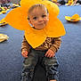 toddler, child, yellow_flower_headpiece, costume, indoor, blue_carpet, craft_activity, group, people, sitting, casual_clothing, jeans, brown_sweater, playful, smiling, faces, women, baby, event, fun