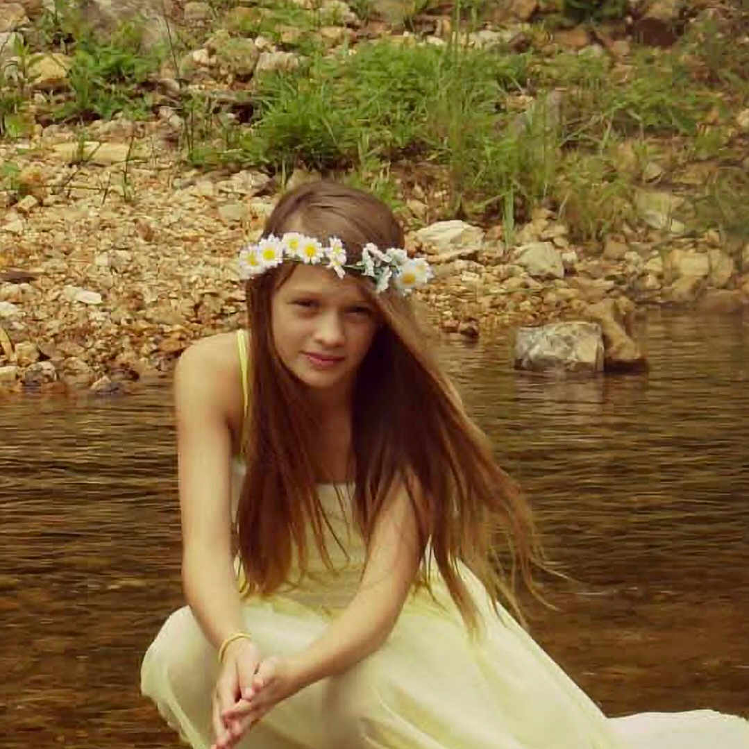 Grace is registered to the contest to win money with this photo: child, girl, flower_crown, yellow_dress, long_hair, water, shallow_water, rocks, grass, nature, outdoor, portrait, serene, crouching, summer, river, fairy_tale, calm, young, fashion