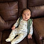 baby, infant, child, onesie, vest, brown_leather_couch, seated, indoor, cute, portrait, comfortable, quilted_fabric, patterned_clothing, small_hands, face, looking_at_camera, home_interior, soft_lighting, relaxed, young