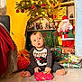 toddler, child, christmas_tree, christmas_lights, gifts, presents, holiday_decorations, santa_figurine, floor, indoor, festive, curious, sitting, red_baubles, tinsel, holiday, cozy, decor, toy, winter