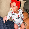 baby, sleeping, pacifier, red_headband, onesie, i_love_mom, tattoo, lap, person, indoor, cushion, clothing, socks, cute, child, infant, resting, peaceful, headwear, human
