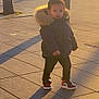 toddler, child, puffy_jacket, hood, sneakers, shadow, sunlight, urban, pavement, outdoor, street, curious, standing, winter_clothing, person, daylight, casual, young_child, cozy, golden_hour