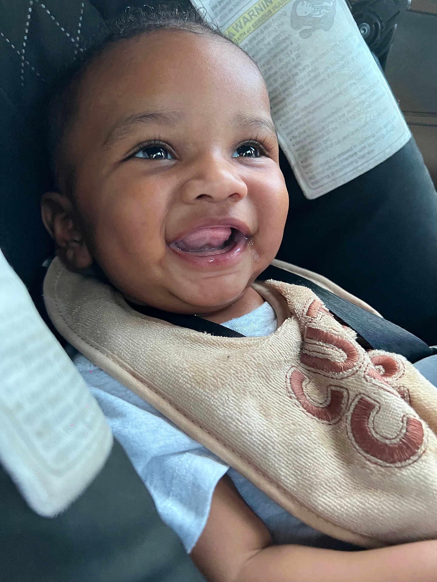 Kyrie is registered to the contest to win money with this photo: baby, smiling, car_seat, bib, happy, child, infant, portrait, clothing, seatbelt, face, cute, young, skin, person, closeup, expression, joyful, indoors, comfort