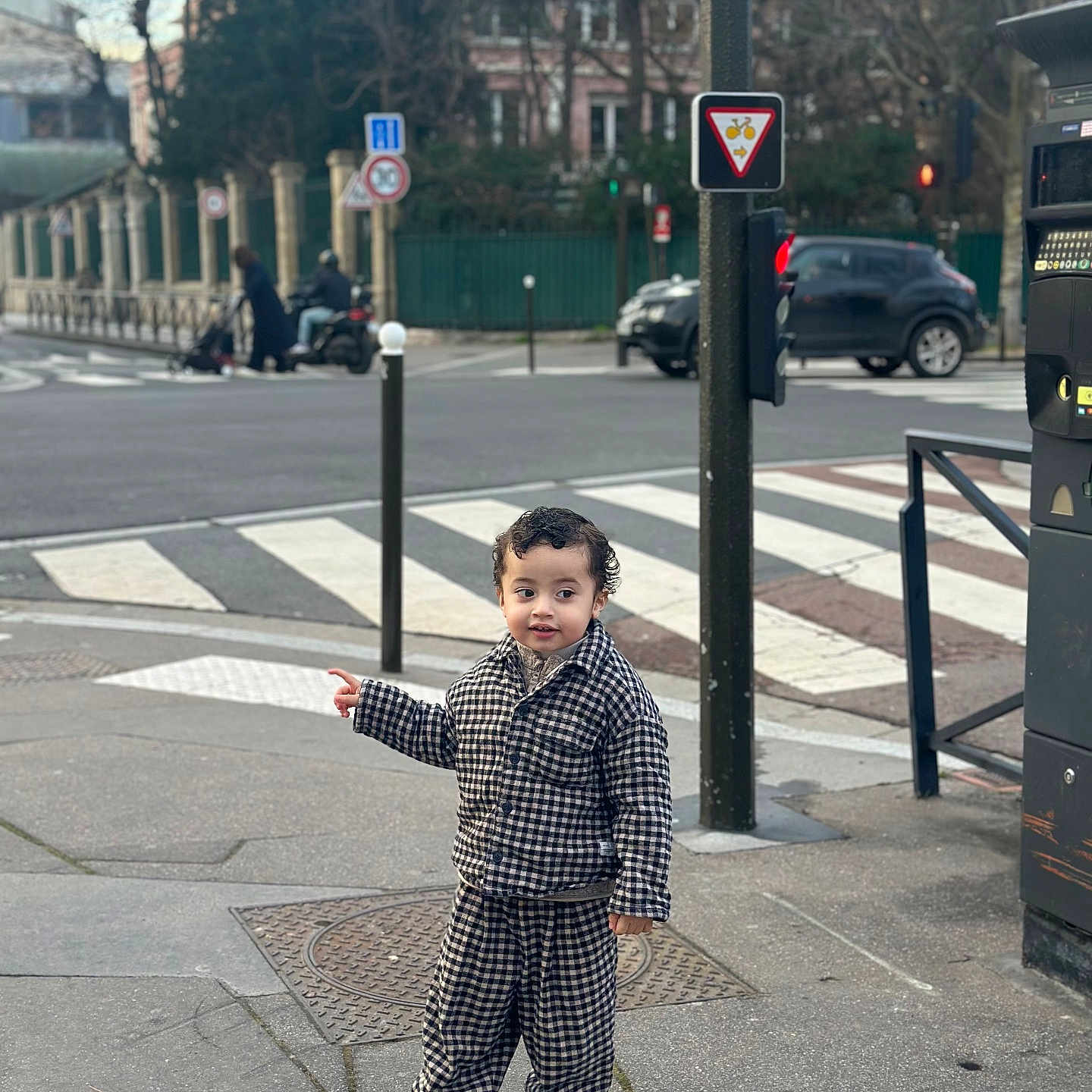 Kiran participe au concours pour gagner de l'argent avec cette photo : car, checkered_outfit, child, city, clothing, concrete, crosswalk, curly_hair, daytime, footwear, metal_pole, outdoor, pedestrian, pointing, sidewalk, street, toddler, traffic_light, traffic_sign, urban