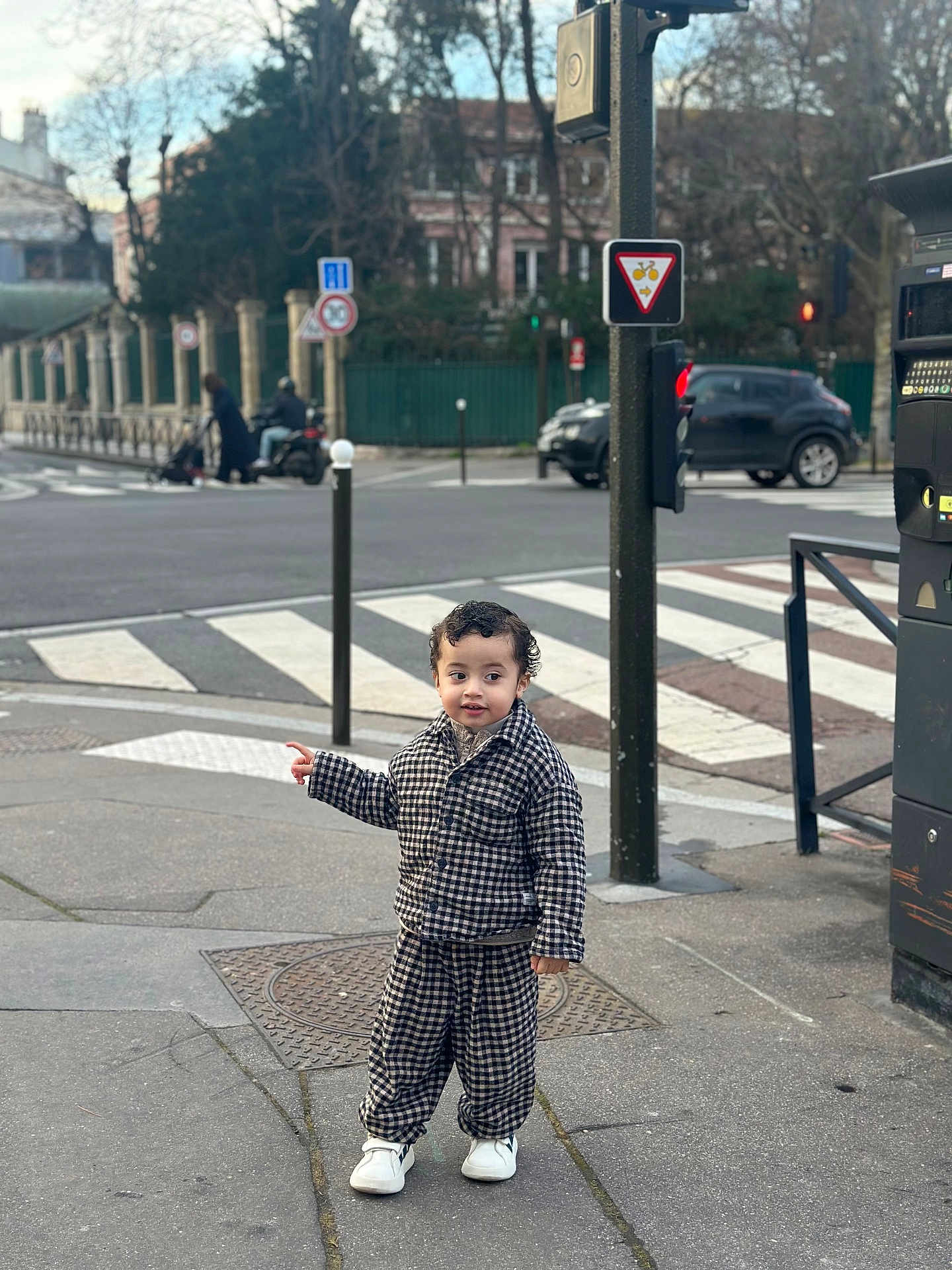 Kiran participe au concours pour gagner de l'argent avec cette photo : car, checkered_outfit, child, city, clothing, concrete, crosswalk, curly_hair, daytime, footwear, metal_pole, outdoor, pedestrian, pointing, sidewalk, street, toddler, traffic_light, traffic_sign, urban