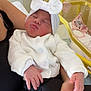 arms, baby, black_pants, blanket, bow, bunny_toy, crib, cute, hand, hospital, indoor, infant, newborn, person, sleeping, soft_lighting, stuffed_toy, white_cardigan, white_headband, yellow_crib