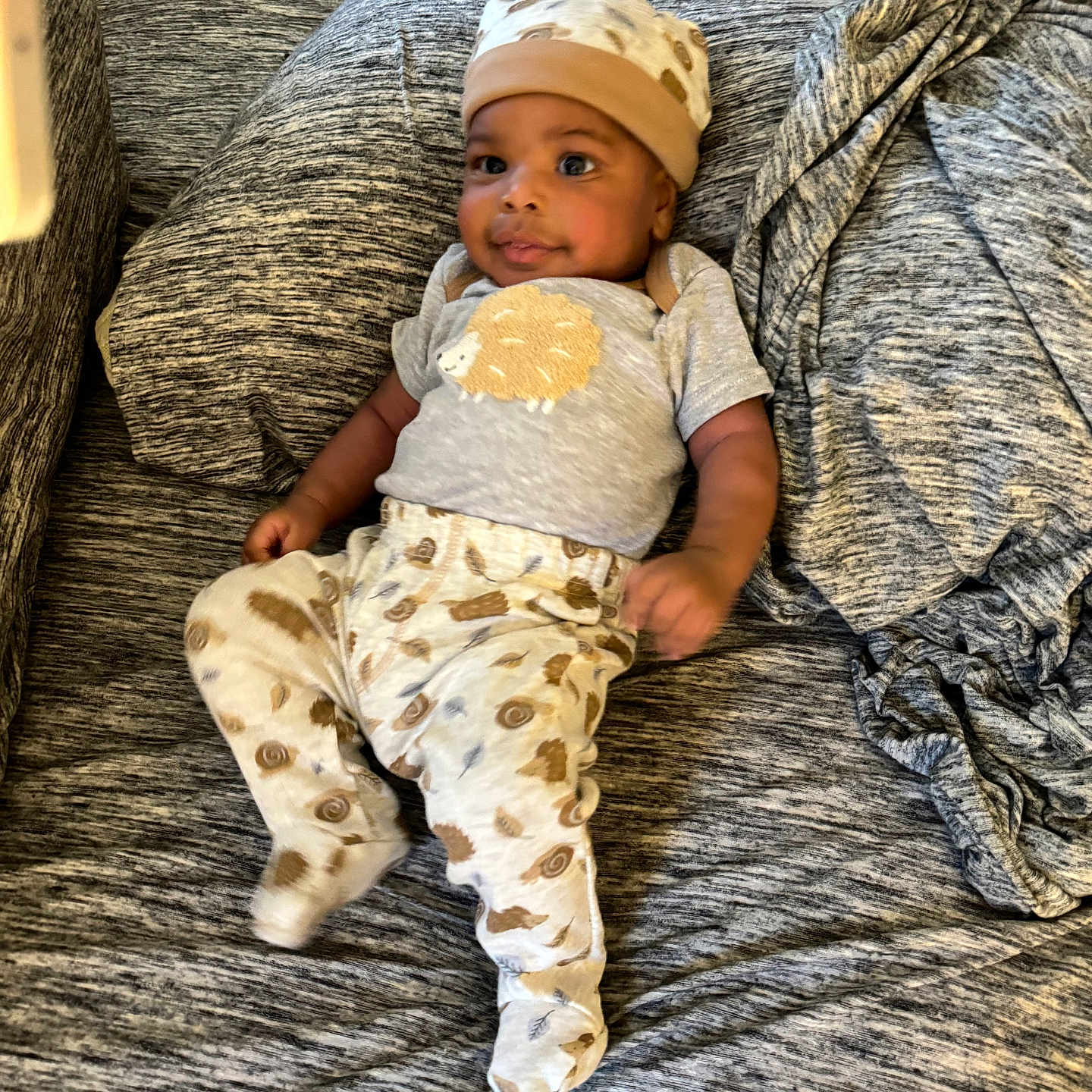 Amier is registered to the contest to win money with this photo: baby, baby_seat, blanket, child, clothing, comfort, couch, cute, fabric, face, hat, indoor, infant, pajamas, pattern, person, relaxed, resting, smile, soft